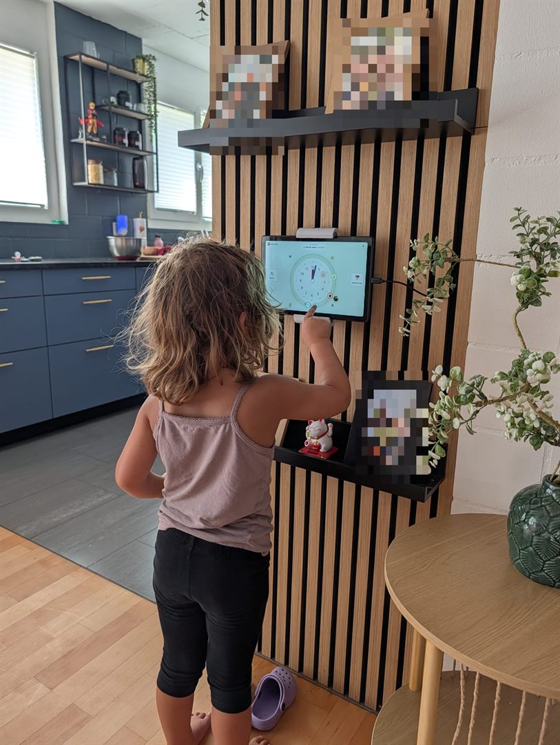 Ein Kind steht in der Küche an der Wand-Lernuhr und tippt seinen nächsten Routine-Schritt selbst an